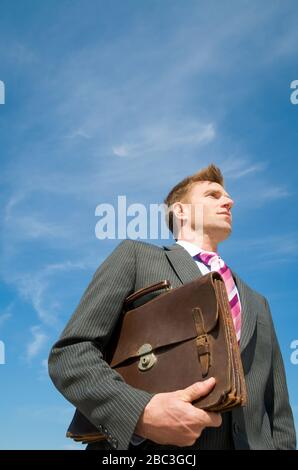 Businessman standing outdoors holding briefcase in sunny blue sky Stock Photo