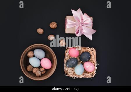 Bright easter greeting background with dyed multicolored chicken quail eggs on straw in plate on black background Stock Photo
