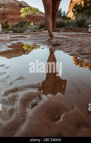 reflection in puddle of woman's legs walking in flipflops in desert mu Stock Photo