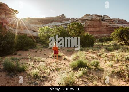 woman walks away as sun sets over the canyon walls in a desert oasis Stock Photo