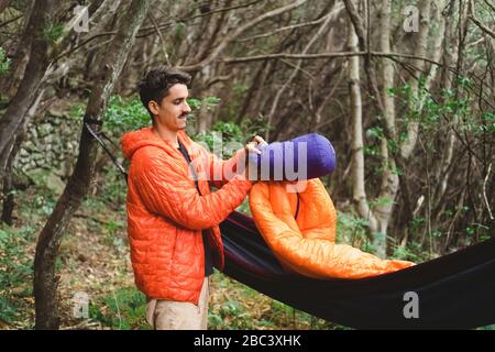 A man packs a sleeping bag and hammock at campsite in the forest Stock Photo