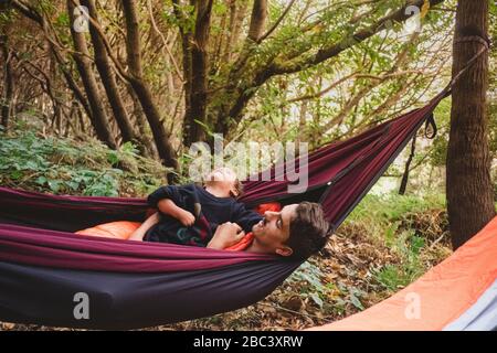 A man and a young kid lying in a hammock in the forest Stock Photo