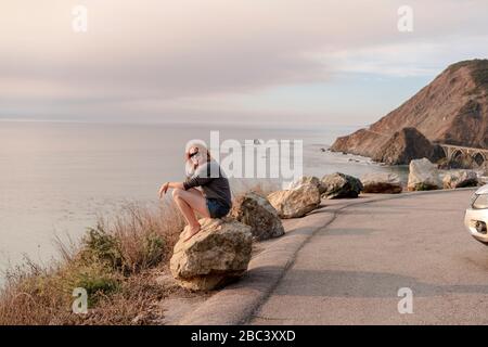 Woman sitting on rock at Big Sur View point Stock Photo