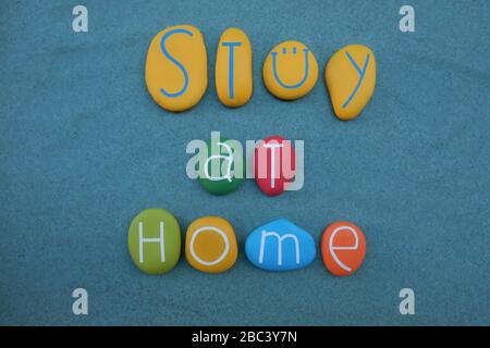 Stay at home text composed with multi colored stone letters over green sand Stock Photo