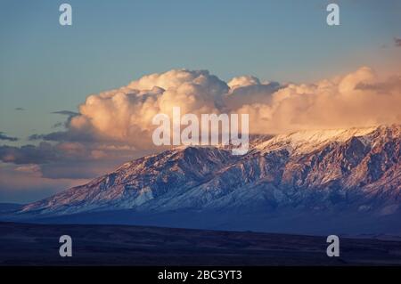 clouds billow over the northern end of the snowy White Mountains in Eastern California at sunset Stock Photo