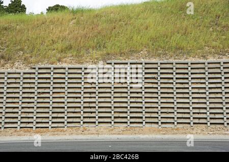 concrete crib retaining wall with grassy slope above it protecting a road Stock Photo