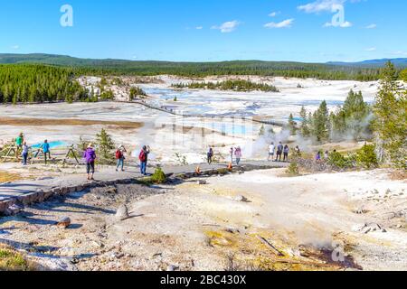 Unrecognizable visitors walking on the Porcelain Basin boardwalk trail surrounded by geothermal pools inside Norris Geyser Basin of Yellowstone Nation Stock Photo