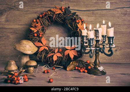 Autumn wreath and still life with ancient candelabrum candle stick , candles with flame. Wooden mushrooms and berries on wood. Design for a seasonal b Stock Photo