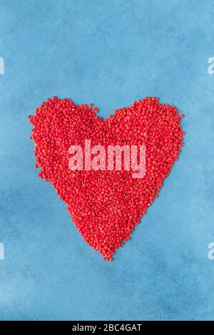 Red lentils scattered on the surface in the form of a heart. Blue background Stock Photo