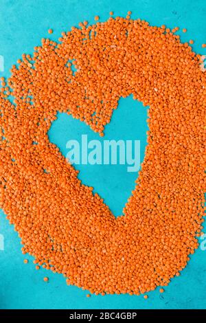 Red lentils scattered on the surface in the form of a heart. Blue background Stock Photo