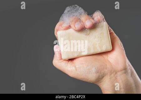 Caucasian male hand holding plain bar of soap with lather and bubbles Stock Photo