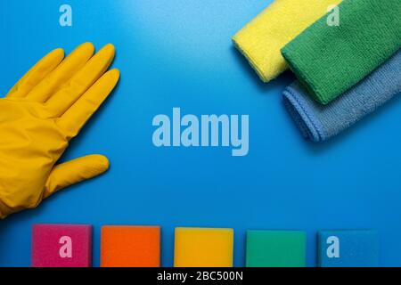 A hand in a yellow rubber glove, three colorful, dry microfiber cloths and rainbow colored sponges for cleaning various surfaces in the kitchen, bathr Stock Photo