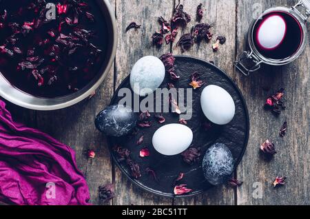 Dyed Easter eggs with marble stone effect painted with natural dye carcade tea from hibiscus flowers on old wooden background. Process of dyeing eggs Stock Photo