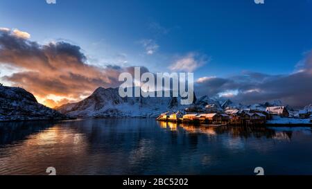 Late afternoon light shining on the coastal buildings, with reflections in the water and snowcapped mountain at background. Stock Photo