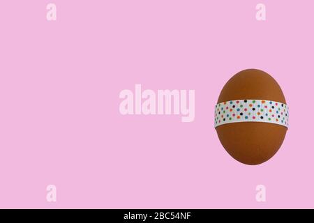 Egg standing on cup, on a soft pink background. Easter egg tied with a festive ribbon. Stock Photo