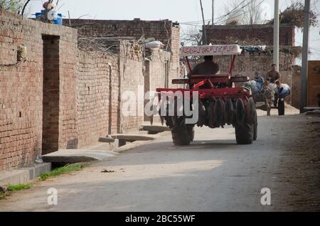 A farmer drives through a village street with his mechanized disc plougher in district Sharaqpur of Punjab province. Stock Photo