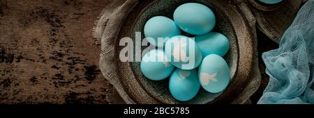 Banner with unusual Easter on dark old background. Ceramic brown bowl with blue eggs with rabbit. Stock Photo