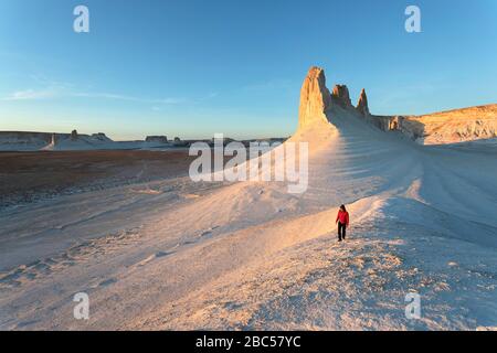 Woman in red jacket walking at rock formations, limestone mountains, Ustyurt, Boszhira, Caspian Depression desert, Aktau, Mangystau, Kazakhstan Stock Photo