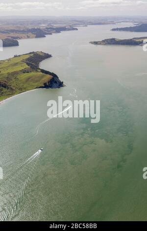 Aerial view on Kaipara Harbour owith a motorboat on clear water in Northland, New Zealand. The landscape shows some coastline extending till the end a Stock Photo