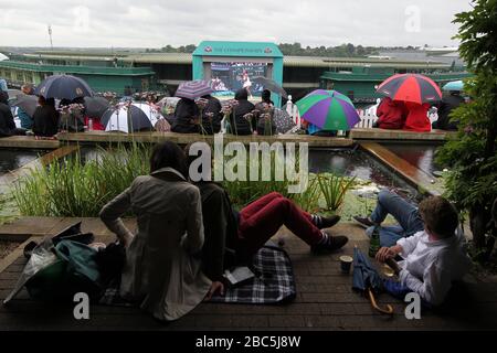 Fans with umbrellas during a rain delay watch the action from centre court on the big screen on Murray Mount Stock Photo