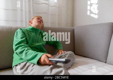 Tired young boy watching tv and falling asleep on the couch at home Stock Photo