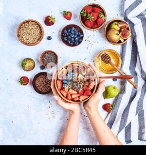 Top view showing hands eating porridge with honey nuts, blueberries on white wooden table selective focus, blurred background Good morning - healthy b Stock Photo