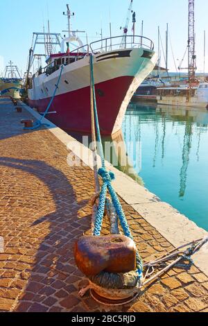 Old trawler moored by bollard on canal in Rimini, Italy Stock Photo