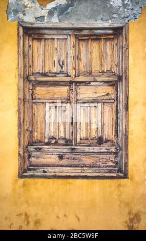 Old wooden closed window in yellow painted wall. Stock Photo