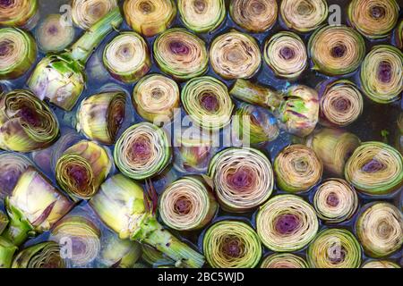 Artichokes in water. Vegetables for sale at an Italian market. Vegetarian background. Stock Photo