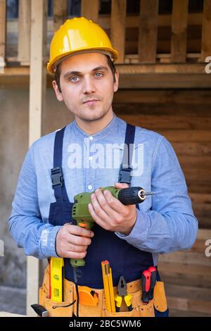 Portrait of a handsome young craftsman with yellow hard hat holding an electric drill Stock Photo