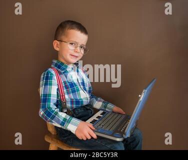 Portrait of a cute serious boy using a notebook. Child in glasses with a laptop. Smart kid tells us about science. Stock Photo