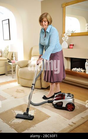 Older woman vacuum cleaning in her lounge at home. Excessive cleaning  can be a sign of OCD, Obsessive Compulsive disorder. Stock Photo