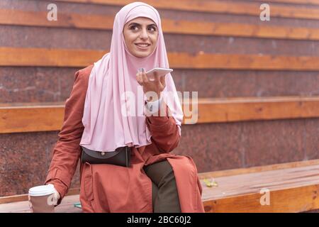 Cheerful young lady sending voice messages at the stadium stock photo Stock Photo