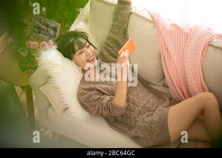 Young Chinese woman playing mobile games on sofa Stock Photo