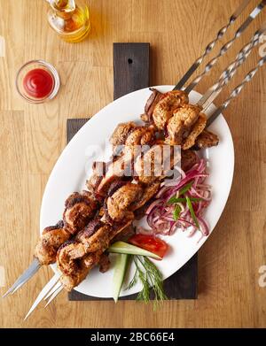 Traditional shashlik on a barbecue skewer near tomato sauce and oil on a black wooden board and wooden background top view Stock Photo