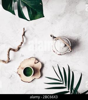 Matcha traditional Japanese powdered green tea in cup near teapot and plants during tea ceremony chado on white marble background Stock Photo
