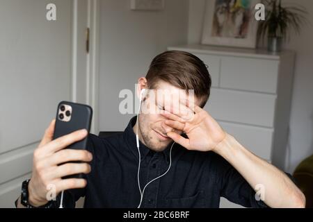 Tired and anxious man having a Zoom video conference call via smartphone. Home office. Stay at home and work from home concept during Coronavirus Stock Photo