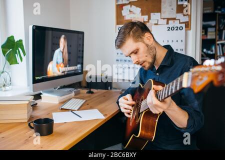 Man learning how to play guitar from online tutorial. Man playing acoustic guitar. Stay at home concept during Coronavirus pandemic. Stock Photo