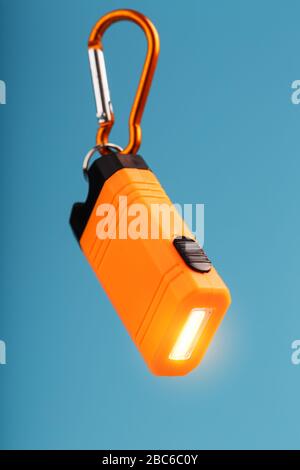 Orange led Flashlight with a carabiner on a blue background. LED lights in flight. Stock Photo