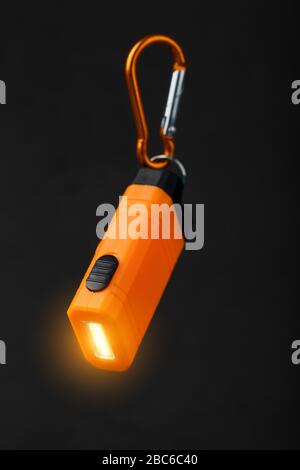 Orange led Flashlight with a carabiner on a black background. LED lights in flight. Stock Photo