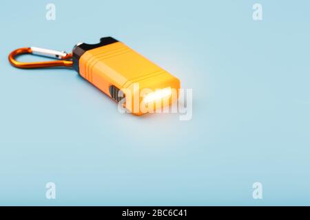 An orange led flashlight with a carabiner glows on a blue background. Stock Photo