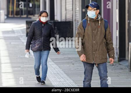 Pictured: A man and a woman walk in the city centre with face masks, Swansea, Wales, UK. Tuesday 31 March 2020 Re: Covid-19 Coronavirus pandemic, UK. Stock Photo