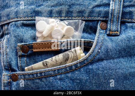 a hundred dollar banknote and pack of white pills sticking out from front pocket of jeans - close-up Stock Photo