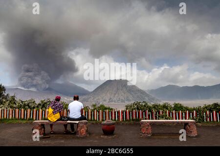 Two Tourists Watching A Mt Bromo Eruption, Bromo Tengger Semeru National Park, Java, Indonesia. Stock Photo