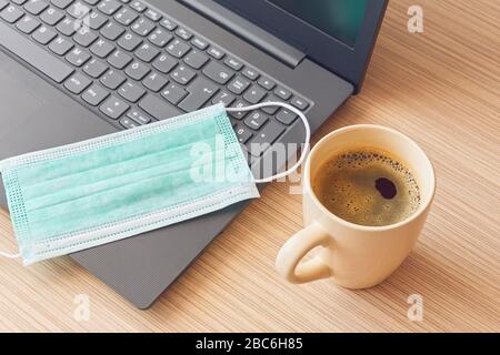 Work from home during coronavirus pandemic, protection mask on notebook and coffee mug Stock Photo