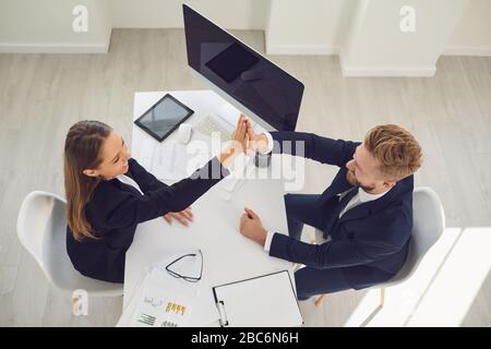 Smiling happy businessmen give high five while sitting at the table at the workplace in the office Stock Photo