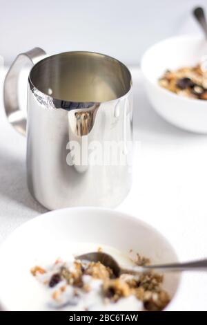 A Jar of Milk and Bowls of Cereals  on White Table Background. Eating Granola. Healthy Breakfast Food. Stock Photo