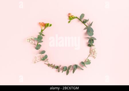 Round frame made of eucalyptus, freesia and gypsophila. Floral wreath on a pink background. Stock Photo