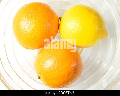 Two oranges and a lemon in a glass bowl on a white tablecloth Stock Photo