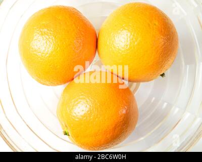 Three oranges in a glass bowl from above on a white tablecloth Stock Photo